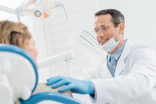Smiling doctor consulting female patient in modern dental clinic Zahnarzt blickt zum Patienten und legt seine Hand auf dessen Schulter