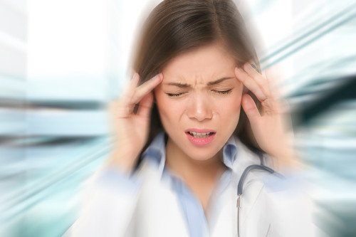 Gestresste Ärztin mit Burnout Ärztin hält sich ihre Finger und Hände an die Schläfe und verzerrt dabei ihr Gesicht.