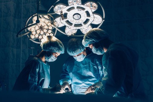 Ärzte im OP-Saal Drei Ärzte stehen in einem OP-Saal und operieren einen Patienten.