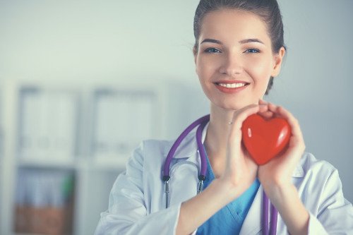 Ärztin hält Herz in Händen Ärztin hält rotes Herz in Händen und lächelt.